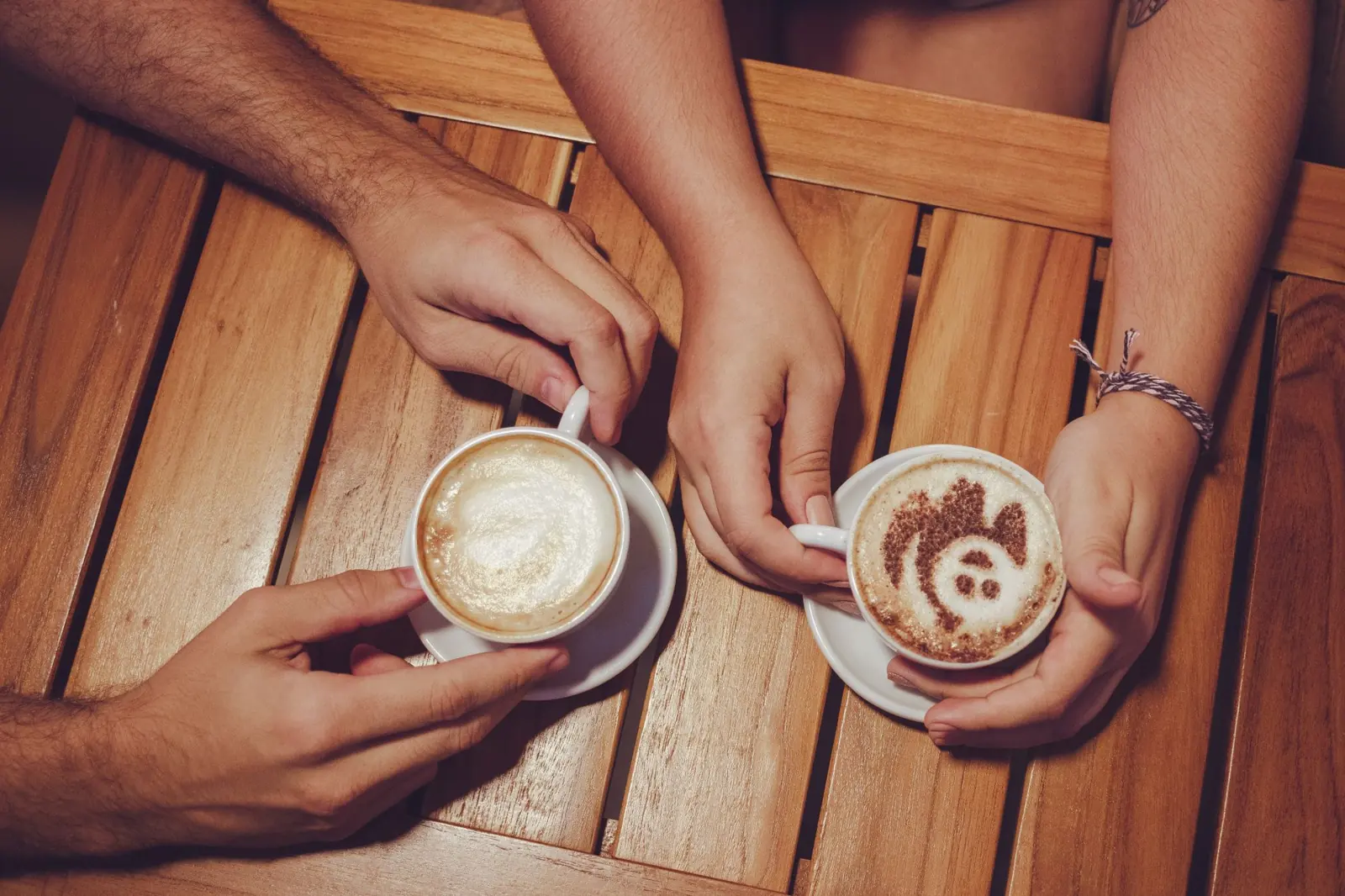 Zwei Hände mit Kaffeetassen von oben, am Holztisch
